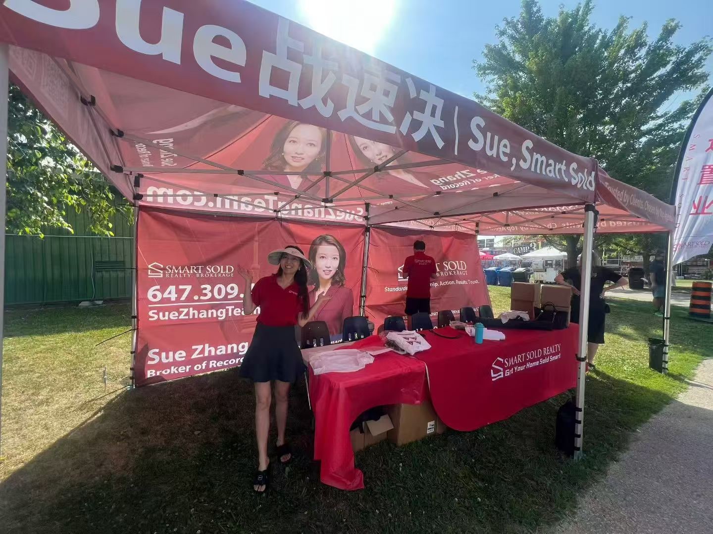 An outdoor Smart Sold Realty booth with a branded tent, table and backdrop featuring Sue Zhang.